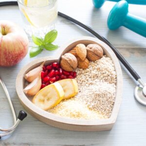 Healthy food in a heart shaped bowl with dumbbells and a stethoscope around it